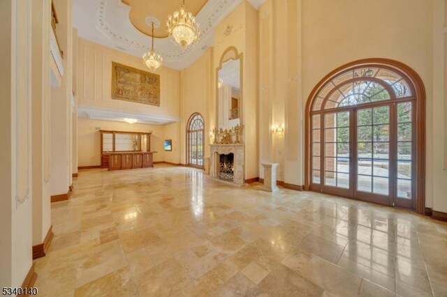 unfurnished living room with baseboards, a high ceiling, french doors, a fireplace, and a notable chandelier