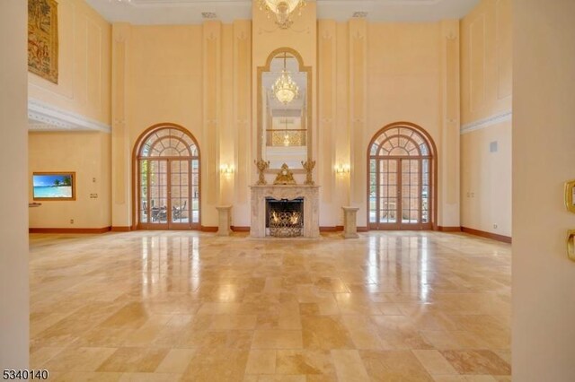 unfurnished living room featuring a towering ceiling, an inviting chandelier, a lit fireplace, and baseboards