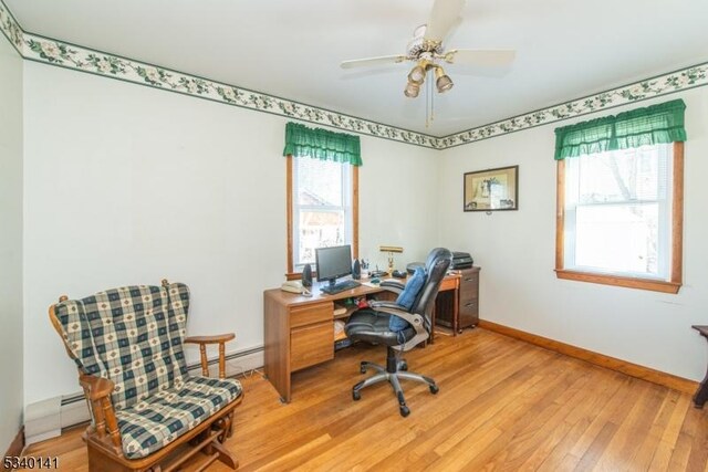 office space with ceiling fan, a baseboard heating unit, light wood-type flooring, and baseboards