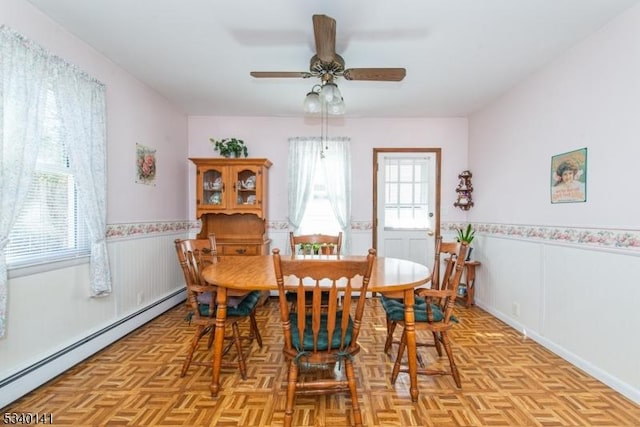 dining space featuring a ceiling fan, baseboard heating, and wainscoting