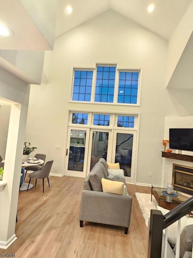 living room featuring high vaulted ceiling, a glass covered fireplace, light wood-style flooring, and baseboards