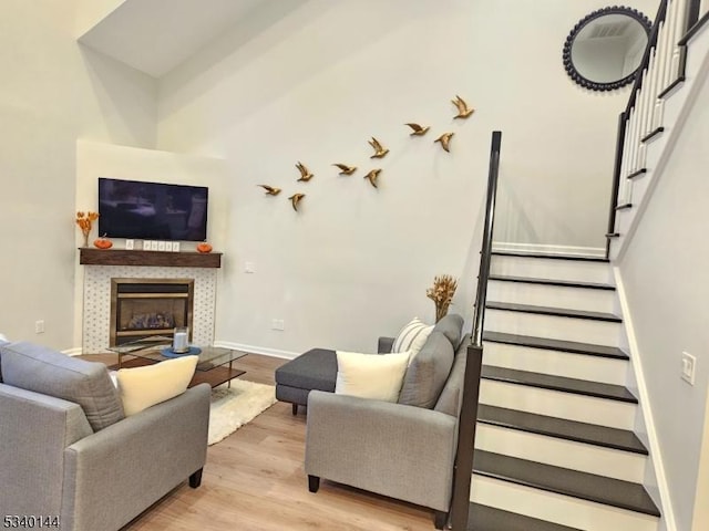 living area featuring light wood-type flooring, stairs, baseboards, and a tiled fireplace