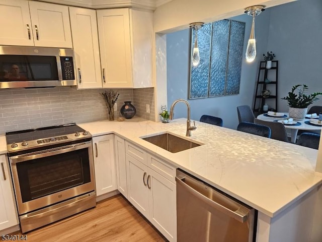 kitchen with stainless steel appliances, a sink, white cabinetry, hanging light fixtures, and light stone countertops