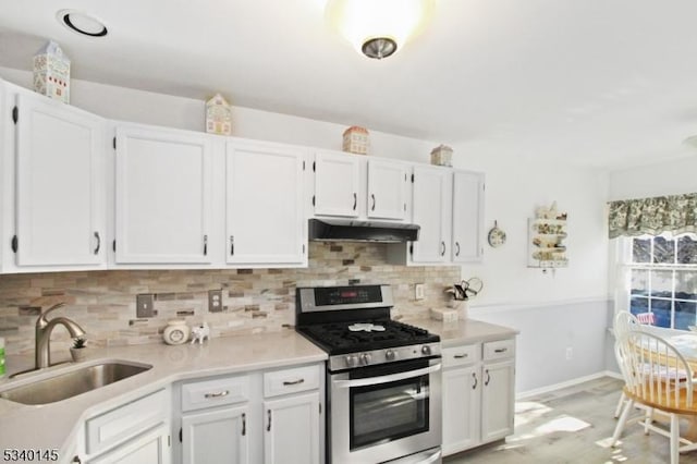 kitchen with under cabinet range hood, a sink, white cabinets, light countertops, and stainless steel gas stove