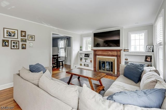 living room with ornamental molding, wood finished floors, a glass covered fireplace, and baseboards