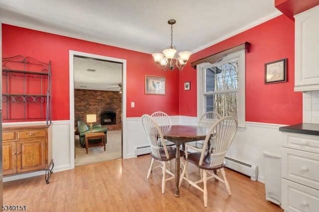 dining room with wainscoting, baseboard heating, a fireplace, and light wood-style floors