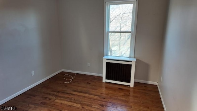 spare room with radiator, baseboards, and wood finished floors