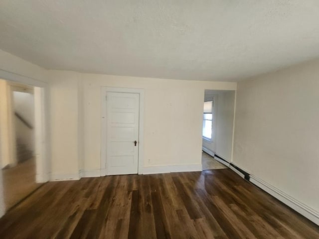 unfurnished room featuring baseboard heating, baseboards, and dark wood finished floors