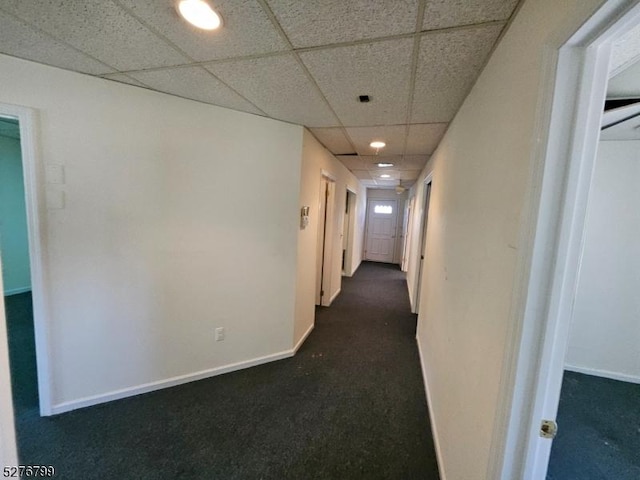 hall featuring dark colored carpet, a paneled ceiling, and baseboards