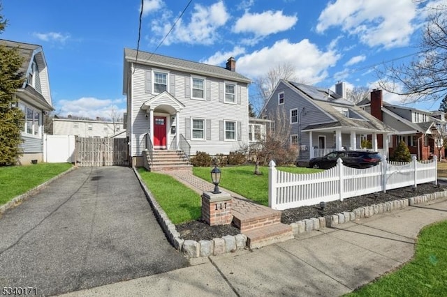 view of front of home with a fenced front yard, aphalt driveway, a chimney, a gate, and a front lawn