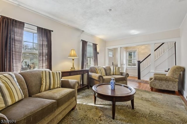 living area with ornamental molding, a textured ceiling, wood finished floors, baseboards, and stairs