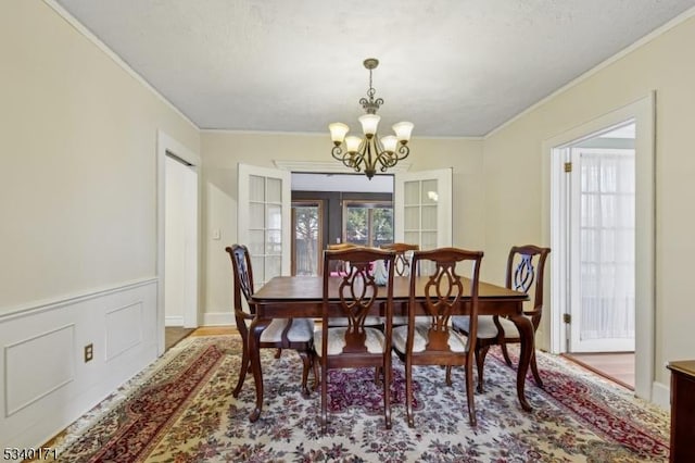 dining space featuring a wainscoted wall, crown molding, a decorative wall, and an inviting chandelier