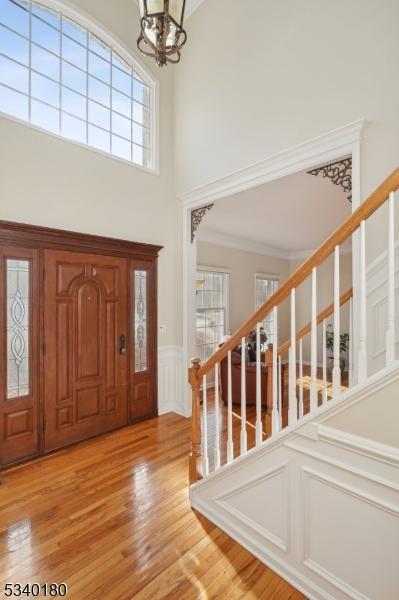 foyer featuring crown molding, stairway, light wood finished floors, and an inviting chandelier