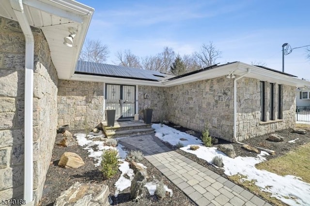 snow covered property entrance featuring stone siding and solar panels