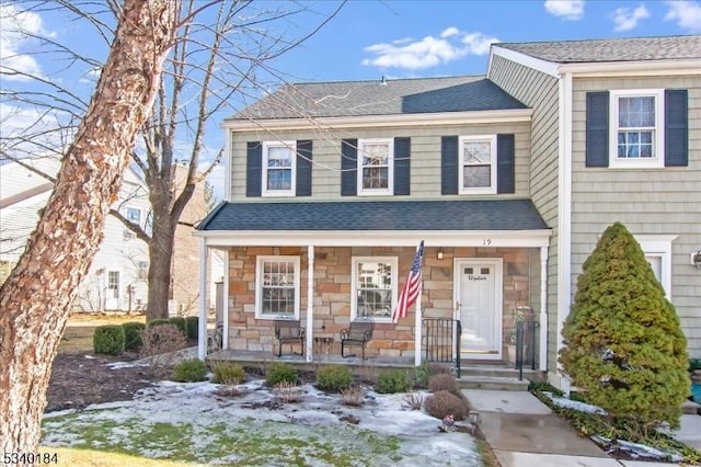 view of front of home with stone siding, covered porch, and roof with shingles