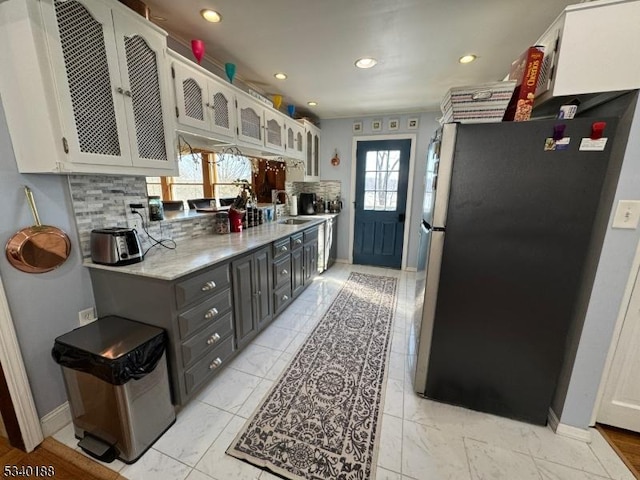 kitchen featuring marble finish floor, glass insert cabinets, freestanding refrigerator, white cabinetry, and a sink