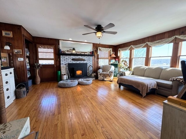 living area with light wood-type flooring, wood walls, ceiling fan, and a fireplace