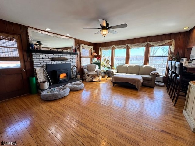 living room featuring a fireplace, recessed lighting, light wood-style flooring, a ceiling fan, and wood walls