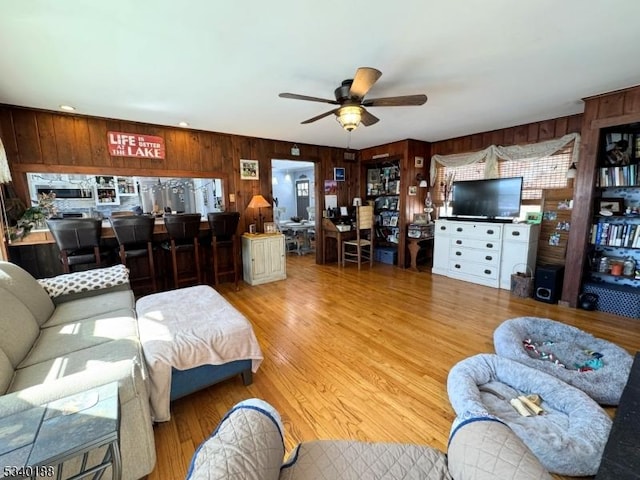 living area featuring a ceiling fan, wooden walls, and wood finished floors