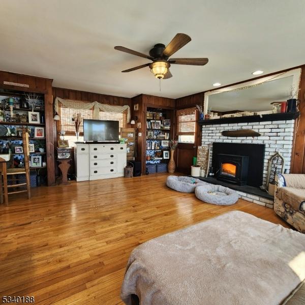 living area featuring ceiling fan, a fireplace, wood finished floors, and wooden walls