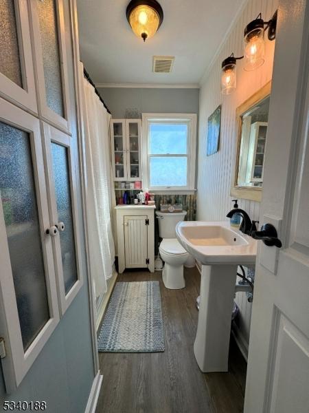 full bathroom featuring crown molding, visible vents, toilet, a sink, and wood finished floors