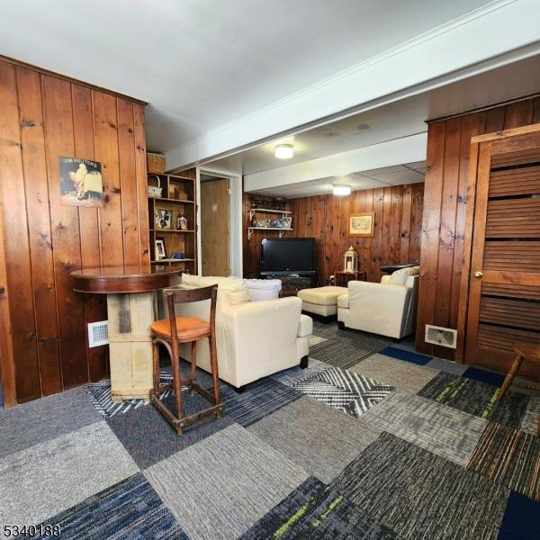 living room with dark colored carpet, visible vents, and wooden walls