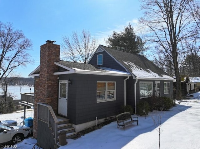 snow covered property featuring roof with shingles and a chimney