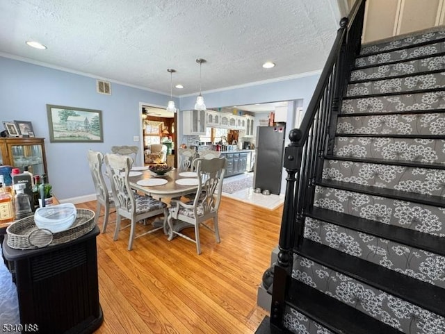 dining area featuring light wood finished floors, visible vents, ornamental molding, a textured ceiling, and stairs