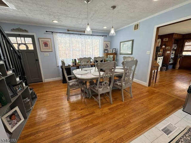 dining area with a textured ceiling, visible vents, baseboards, light wood-style floors, and ornamental molding