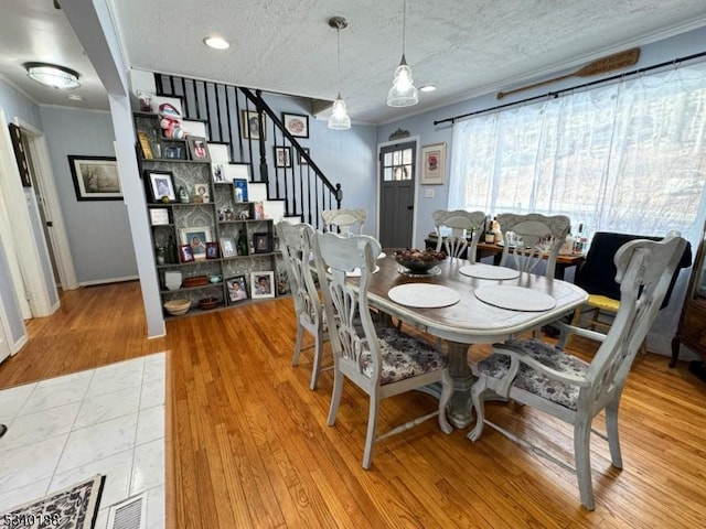 dining room featuring a textured ceiling, ornamental molding, stairway, and wood finished floors