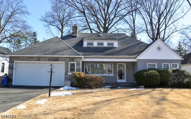 view of front of property featuring driveway, a garage, a shingled roof, stone siding, and a chimney