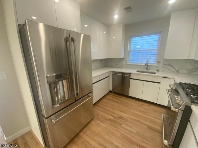 kitchen with a sink, light countertops, white cabinets, light wood-style floors, and appliances with stainless steel finishes