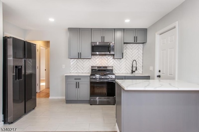 kitchen featuring appliances with stainless steel finishes, tasteful backsplash, gray cabinetry, and light stone countertops