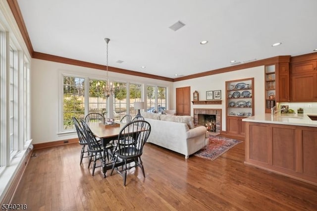 dining room with ornamental molding, a brick fireplace, wood finished floors, and baseboards