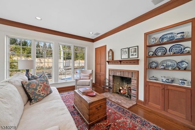 living area featuring built in features, dark wood finished floors, a fireplace, crown molding, and recessed lighting