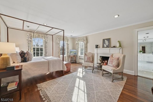 bedroom with dark wood-style floors, a lit fireplace, ornamental molding, and recessed lighting