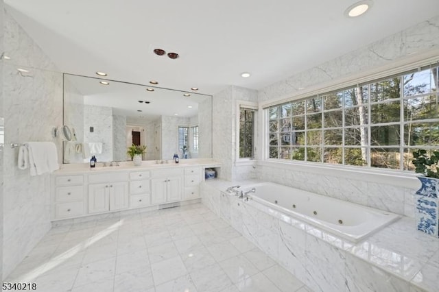 full bath featuring a sink, tile walls, a tub with jets, and double vanity