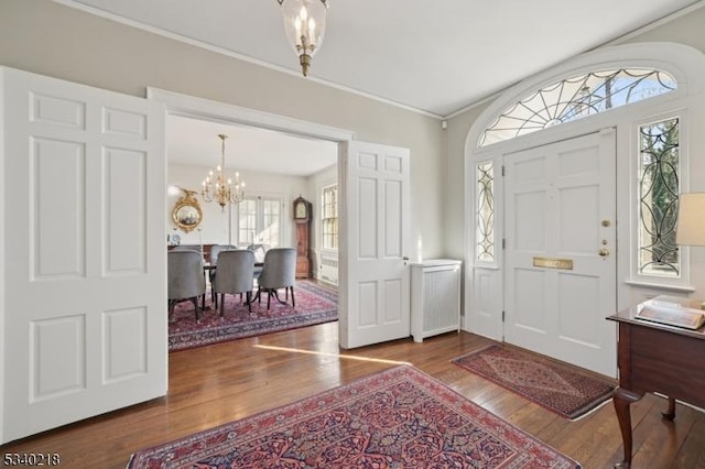 entryway with ornamental molding, dark wood-type flooring, and a notable chandelier