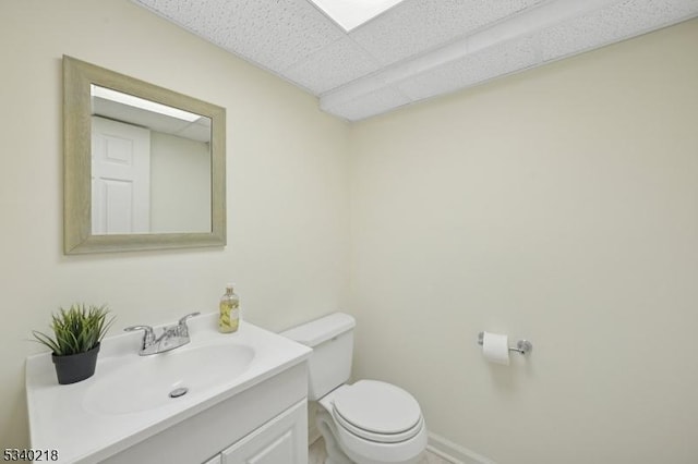 bathroom featuring toilet, a drop ceiling, vanity, and baseboards