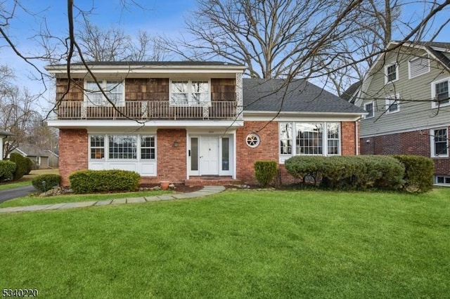 view of front of home featuring a balcony, roof with shingles, a front yard, and brick siding