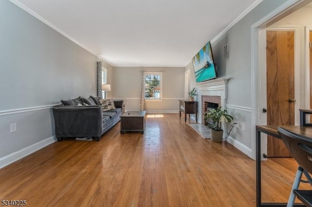 living room featuring baseboards, a fireplace with flush hearth, ornamental molding, and wood finished floors