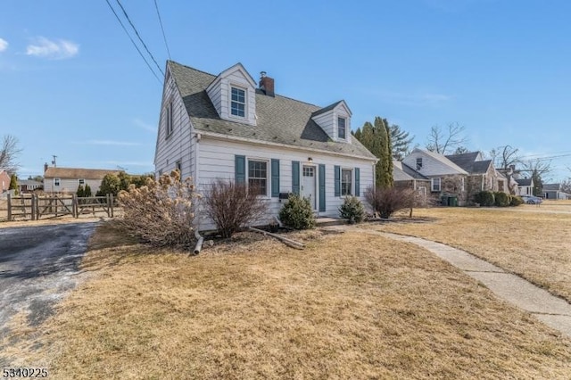 new england style home with a chimney, a front yard, and fence