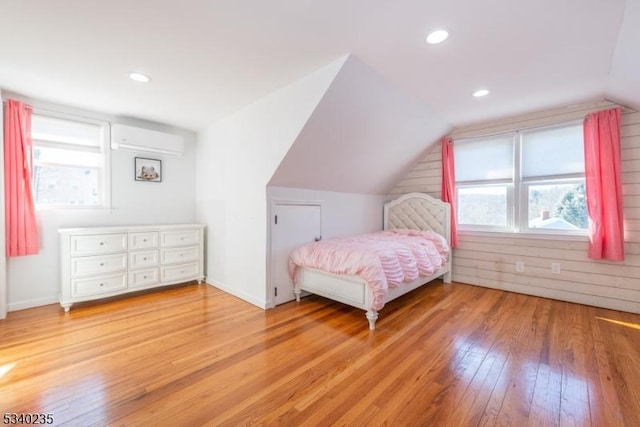 bedroom with multiple windows, vaulted ceiling, a wall mounted AC, and hardwood / wood-style flooring