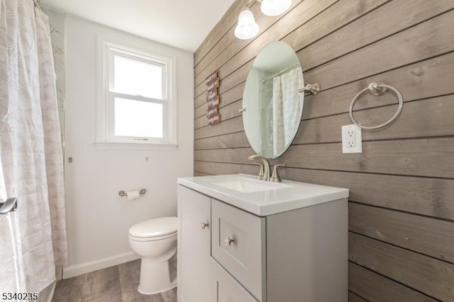 bathroom with wooden walls, baseboards, toilet, wood finished floors, and vanity