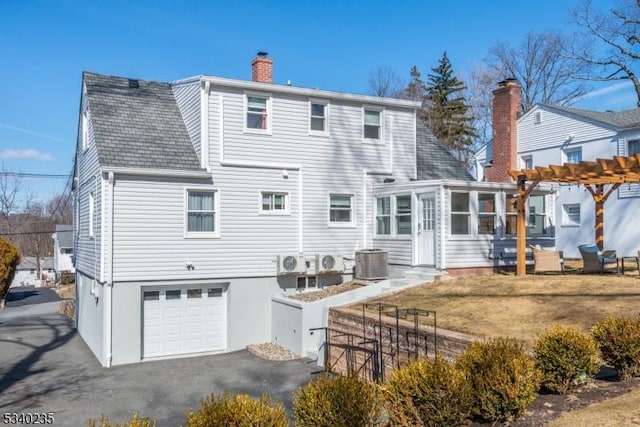 back of property featuring a pergola, a sunroom, a chimney, an attached garage, and central AC