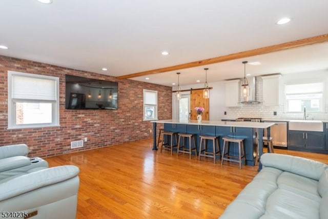 living area with a healthy amount of sunlight, brick wall, and light wood-style flooring