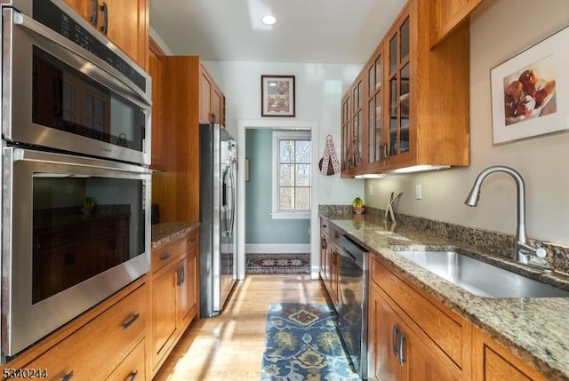 kitchen with stainless steel appliances, light stone counters, brown cabinetry, and a sink