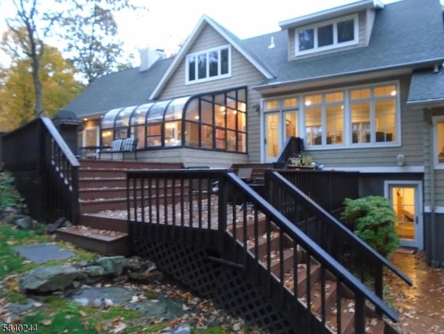 rear view of property with a deck, a sunroom, roof with shingles, and stairway