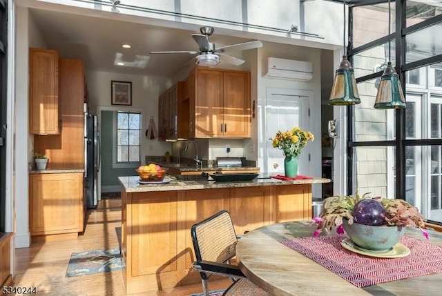 kitchen with a sink, light wood-type flooring, freestanding refrigerator, brown cabinetry, and a wall mounted air conditioner