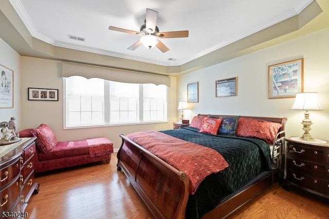 bedroom featuring a ceiling fan, visible vents, wood finished floors, and ornamental molding